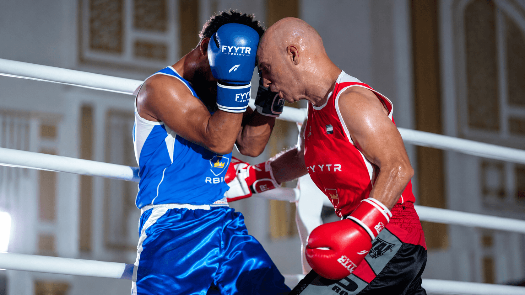 Red and blue corner boxers in a clinch at a UAE fight night